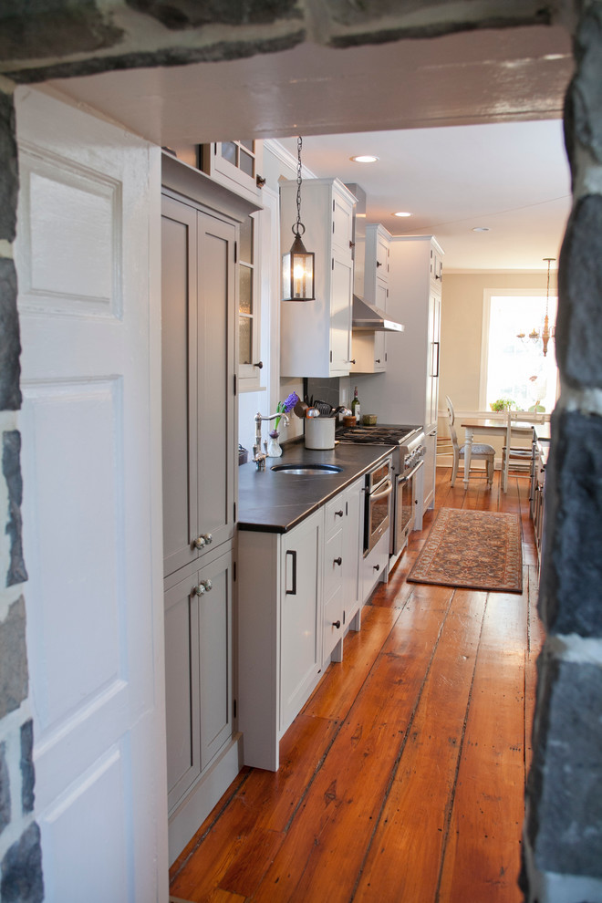 Photo of a large country galley eat-in kitchen in Philadelphia with a farmhouse sink, shaker cabinets, grey cabinets, soapstone benchtops, stainless steel appliances, medium hardwood floors and with island.
