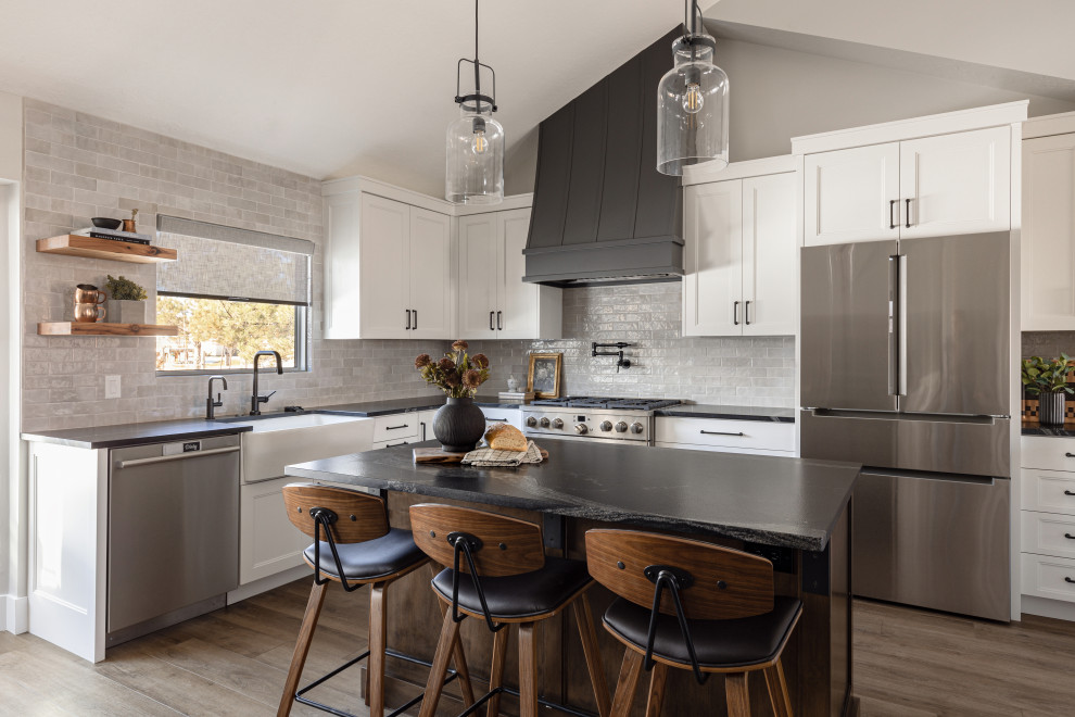 Eat-in kitchen - large transitional u-shaped laminate floor and brown floor eat-in kitchen idea in Salt Lake City with a farmhouse sink, recessed-panel cabinets, white cabinets, granite countertops, gray backsplash, subway tile backsplash, stainless steel appliances, an island and black countertops