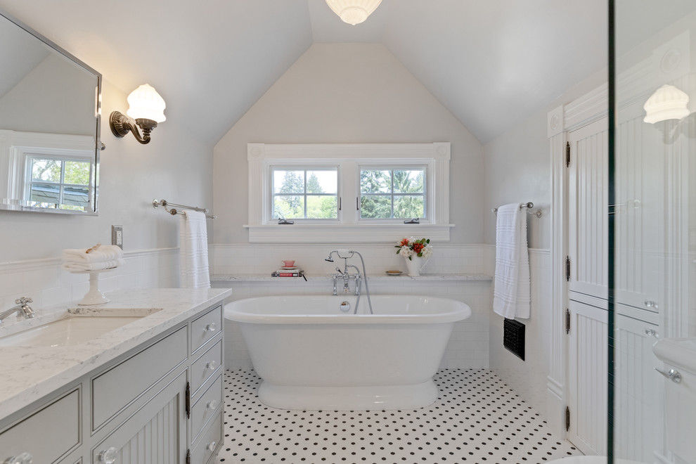 Traditional master bathroom in Portland with grey cabinets, a freestanding tub, a two-piece toilet, white tile, subway tile, grey walls, ceramic floors, an undermount sink, quartzite benchtops, multi-coloured floor, a hinged shower door and white benchtops.