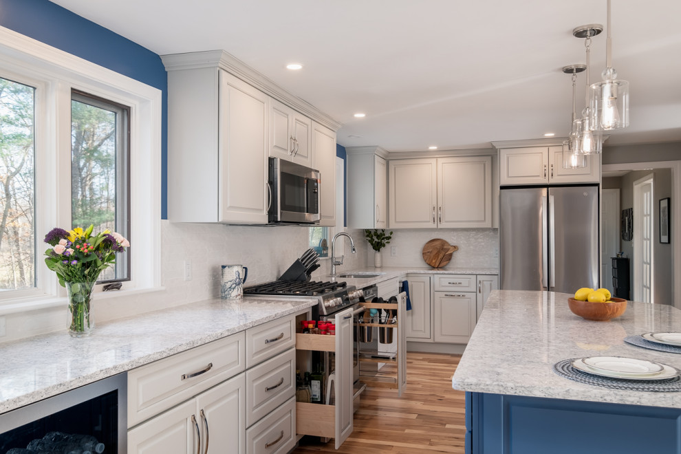 Inspiration for a mid-sized transitional l-shaped light wood floor eat-in kitchen remodel in Boston with a single-bowl sink, raised-panel cabinets, gray cabinets, quartz countertops, white backsplash, ceramic backsplash, stainless steel appliances, an island and white countertops