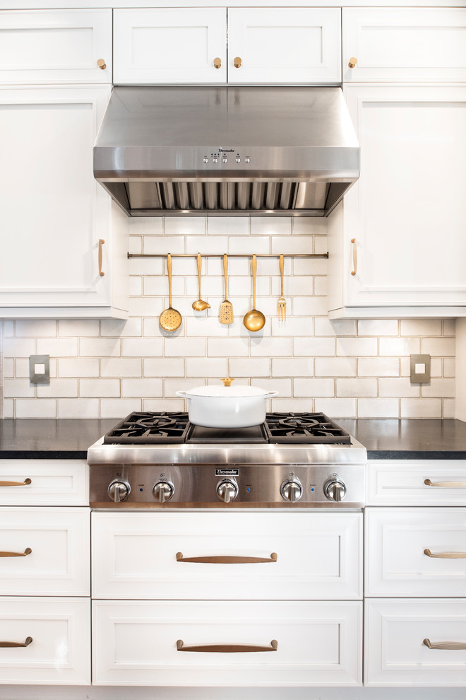 Large transitional u-shaped medium tone wood floor and brown floor eat-in kitchen photo with white backsplash, glass tile backsplash, stainless steel appliances, an island, a farmhouse sink, recessed-panel cabinets, white cabinets and marble countertops