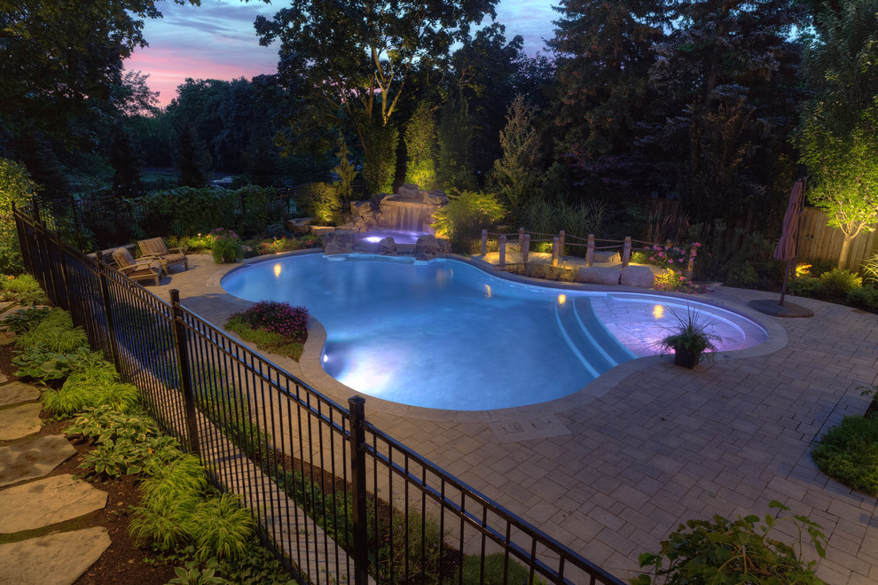 Design ideas for a mid-sized contemporary backyard custom-shaped natural pool in Toronto with a hot tub and brick pavers.
