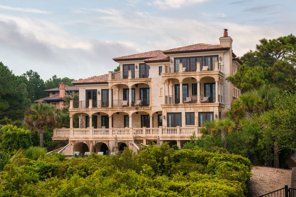 Large mediterranean three-storey stucco beige house exterior in Charleston with a hip roof and a shingle roof.