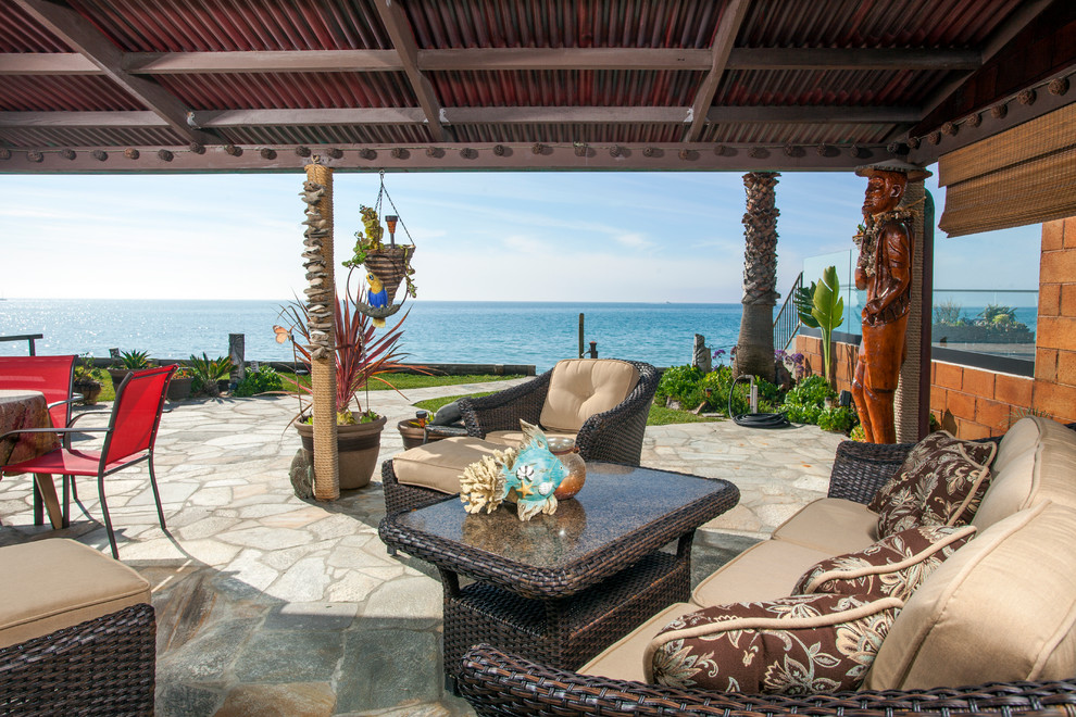 Expansive beach style backyard patio in Orange County with natural stone pavers, a roof extension and a water feature.