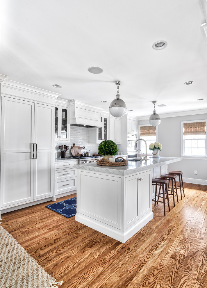 This is an example of a large transitional kitchen in New York with an undermount sink, white cabinets, marble benchtops, white splashback, subway tile splashback, stainless steel appliances, with island, grey benchtop, shaker cabinets and medium hardwood floors.
