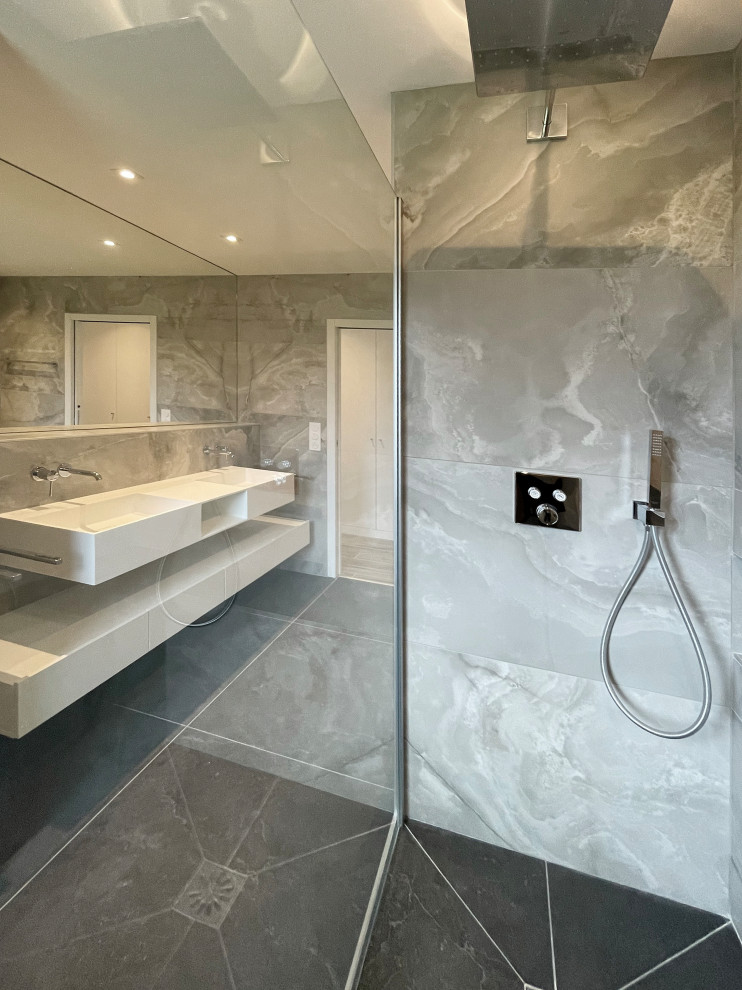 Inspiration för ett mellanstort funkis vit vitt en-suite badrum, med ett badkar i en alkov, en dusch i en alkov, en vägghängd toalettstol, grå kakel, stenkakel, grå väggar, skiffergolv, ett avlångt handfat, bänkskiva i akrylsten och grått golv
