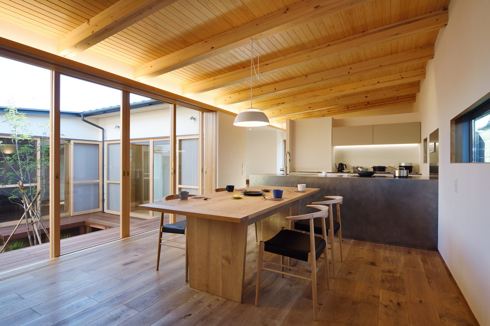 Cette photo montre une grande salle à manger ouverte sur le salon avec un mur blanc, un sol en bois brun, aucune cheminée et un plafond en bois.