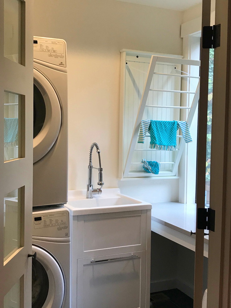 This is an example of a small arts and crafts u-shaped utility room in Seattle with an utility sink, shaker cabinets, white cabinets, quartz benchtops, white walls, slate floors, a stacked washer and dryer, green floor and grey benchtop.