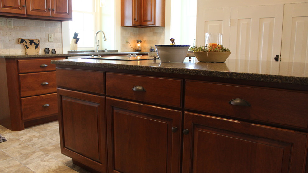 This is an example of a medium sized traditional l-shaped kitchen/diner in Philadelphia with a submerged sink, raised-panel cabinets, medium wood cabinets, engineered stone countertops, beige splashback, ceramic splashback, stainless steel appliances, vinyl flooring and an island.