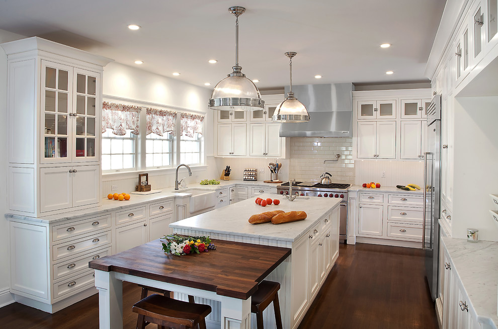 Photo of a mid-sized traditional u-shaped kitchen in New York with a farmhouse sink, beaded inset cabinets, white cabinets, marble benchtops, white splashback, subway tile splashback, stainless steel appliances, dark hardwood floors and with island.