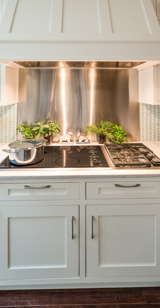 This is an example of a large traditional l-shaped eat-in kitchen in Indianapolis with a farmhouse sink, shaker cabinets, white cabinets, quartz benchtops, blue splashback, mosaic tile splashback, stainless steel appliances, medium hardwood floors and a peninsula.