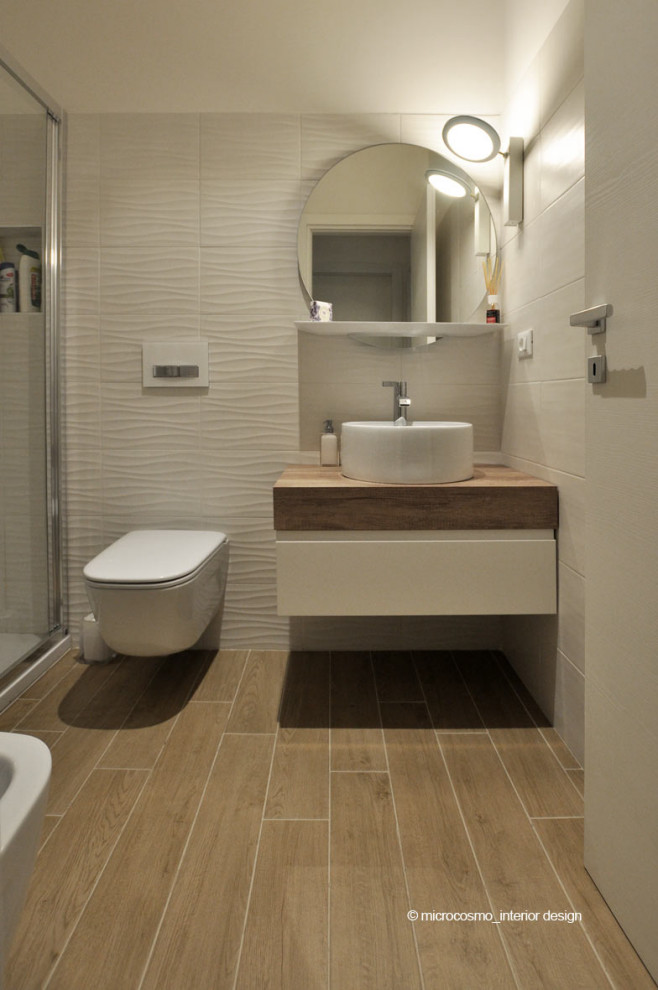 Photo of a small scandinavian 3/4 bathroom in Rome with flat-panel cabinets, white cabinets, a corner shower, a wall-mount toilet, white tile, porcelain tile, white walls, porcelain floors, a vessel sink, wood benchtops, brown floor, a hinged shower door and brown benchtops.