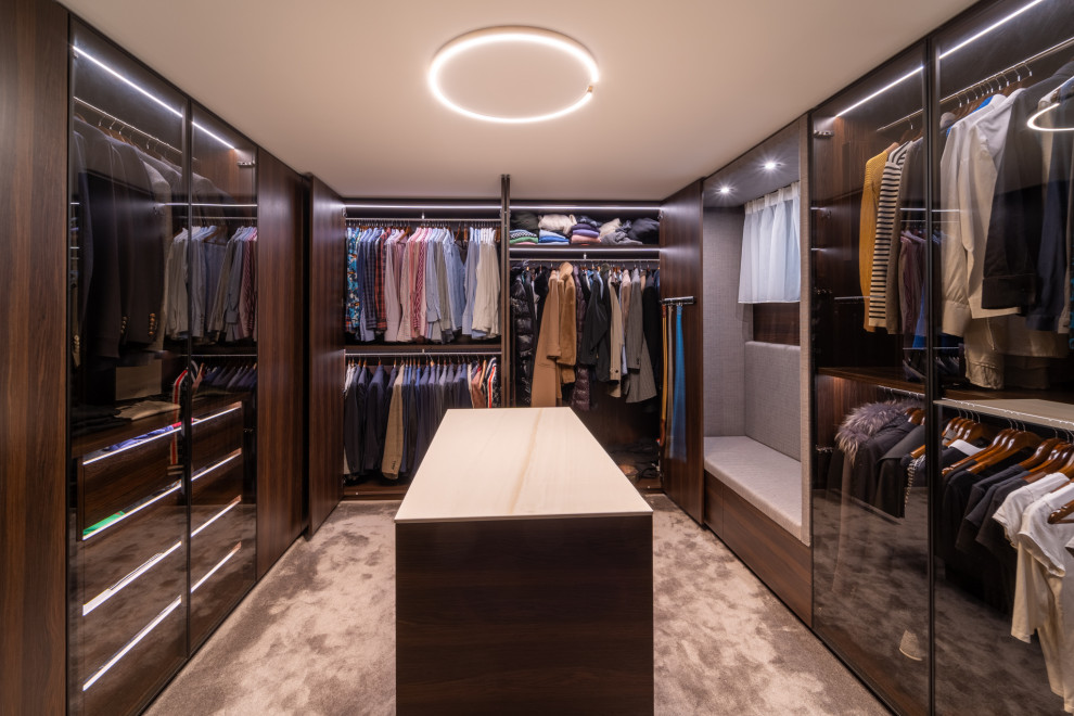 Medium sized modern dressing room in Frankfurt with glass-front cabinets, dark wood cabinets, carpet and grey floors.