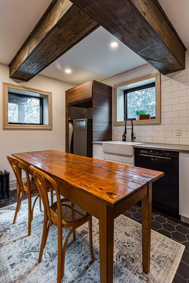 Mid-sized mountain style u-shaped ceramic tile, black floor and exposed beam eat-in kitchen photo in Toronto with a farmhouse sink, flat-panel cabinets, white cabinets, quartz countertops, white backsplash, subway tile backsplash, stainless steel appliances, an island and gray countertops