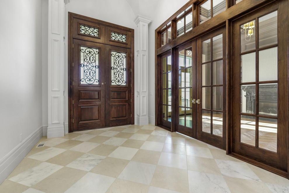 Idée de décoration pour un grand hall d'entrée avec un mur blanc, un sol en marbre, une porte double, une porte en bois foncé, un sol blanc et un plafond voûté.