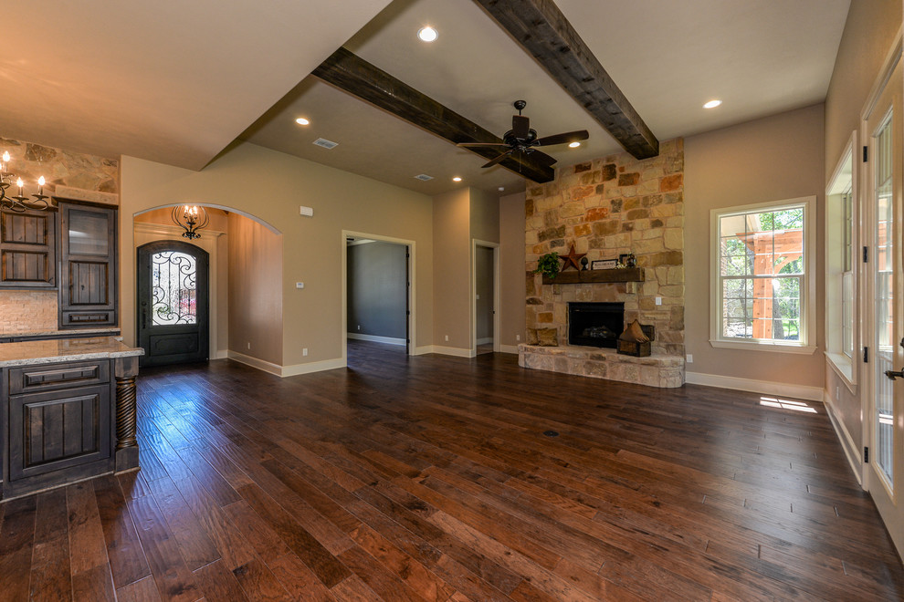 Inspiration for a large country open concept living room in Austin with beige walls, dark hardwood floors, a standard fireplace, a stone fireplace surround and a wall-mounted tv.