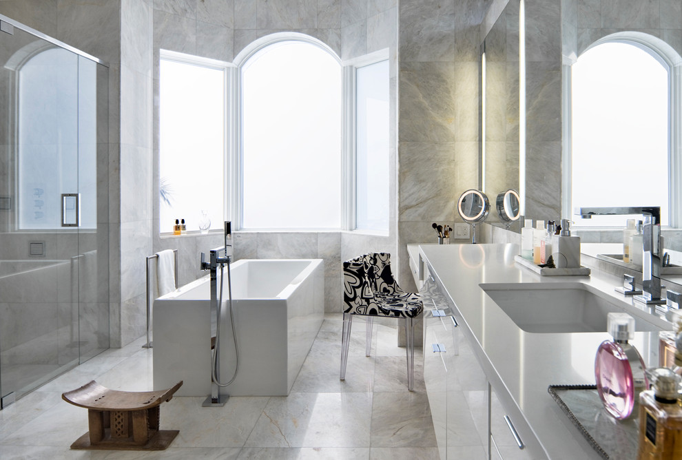 This is an example of a large contemporary master bathroom in Miami with an undermount sink, flat-panel cabinets, white cabinets, a freestanding tub, an alcove shower, gray tile, limestone, grey walls, limestone floors, engineered quartz benchtops, grey floor and a hinged shower door.