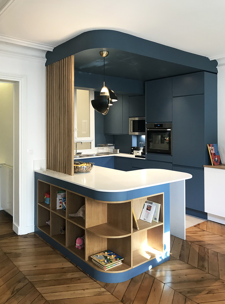 This is an example of a mid-sized contemporary eat-in kitchen in Paris with an integrated sink, beaded inset cabinets, blue cabinets, quartzite benchtops, blue splashback, stainless steel appliances, ceramic floors, with island, grey floor and white benchtop.