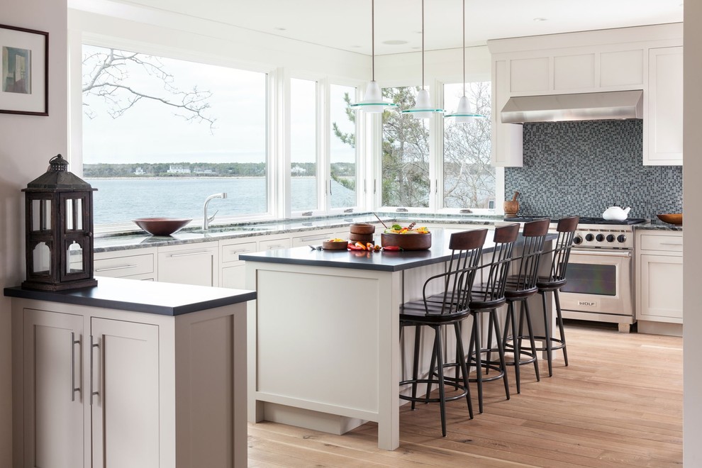 Photo of a beach style u-shaped kitchen in Boston with shaker cabinets, white cabinets, grey splashback, mosaic tile splashback, stainless steel appliances, light hardwood floors, with island and brown floor.