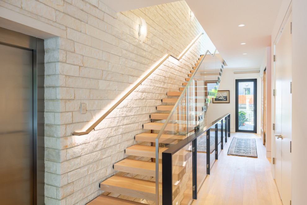 На фото: лестница в современном стиле с деревянными ступенями, стеклянными подступенками, стеклянными перилами и кирпичными стенами с