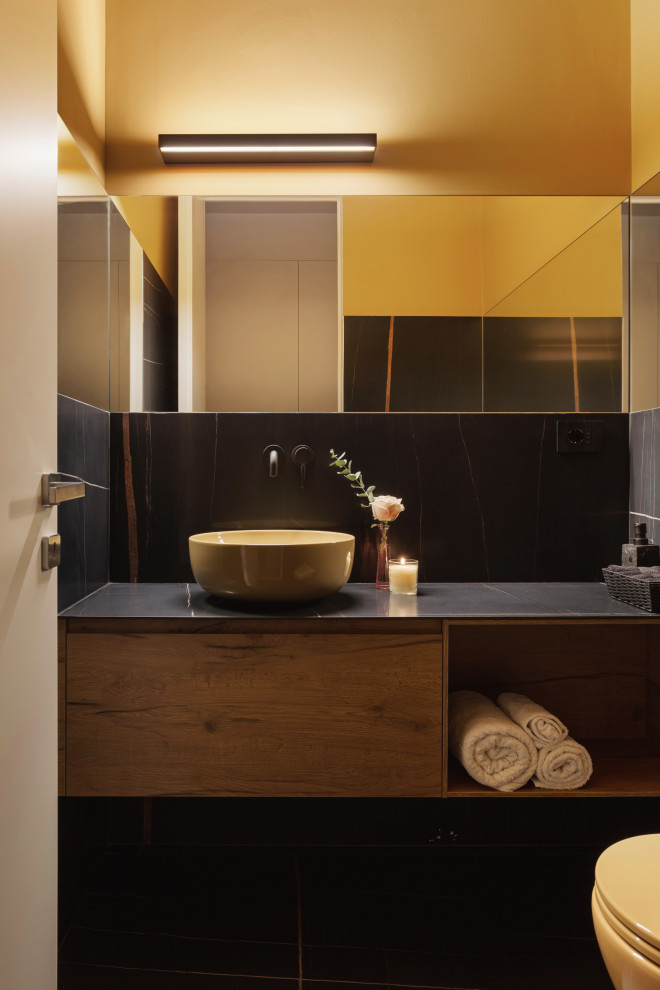 Inredning av ett modernt litet svart svart badrum, med släta luckor, beige skåp, en vägghängd toalettstol, svart kakel, marmorkakel, gula väggar, marmorgolv, ett fristående handfat, marmorbänkskiva och svart golv