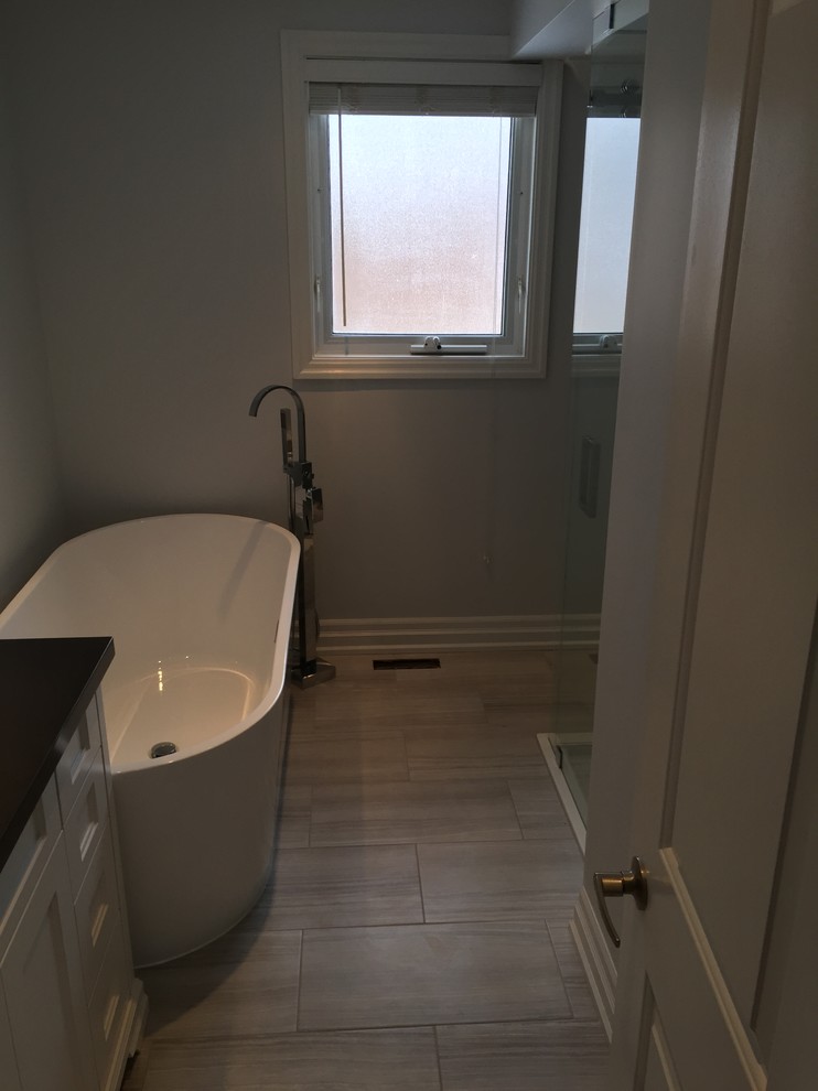 Inspiration for a mid-sized contemporary 3/4 bathroom in Toronto with shaker cabinets, white cabinets, a freestanding tub, a corner shower, a two-piece toilet, gray tile, grey walls, ceramic floors, an undermount sink, granite benchtops, grey floor, a hinged shower door and ceramic tile.