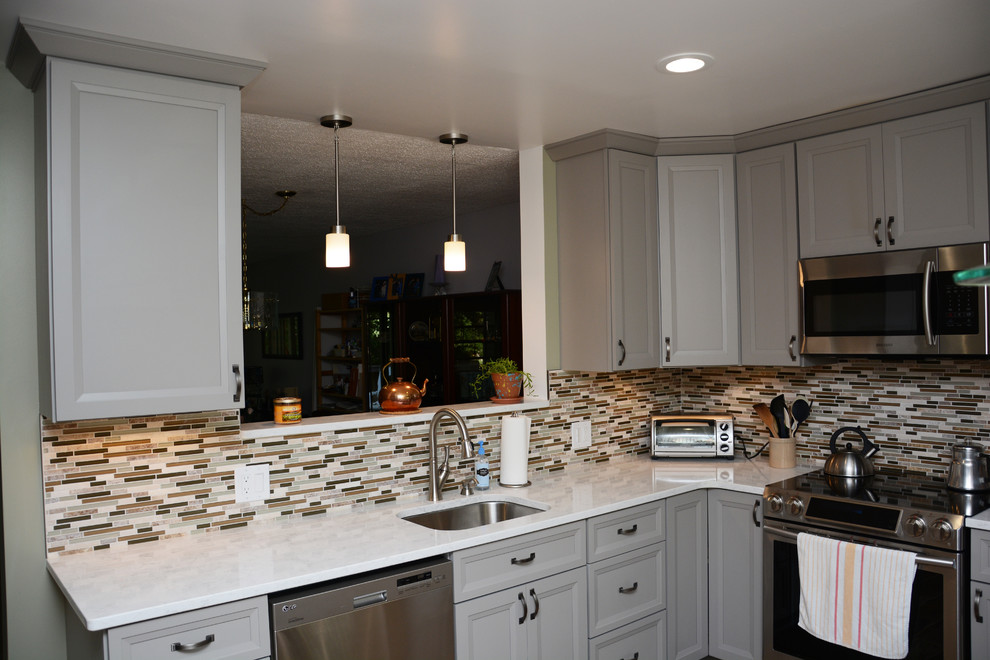 Example of a mid-sized transitional l-shaped medium tone wood floor enclosed kitchen design in DC Metro with a single-bowl sink, recessed-panel cabinets, gray cabinets, quartz countertops, multicolored backsplash, glass tile backsplash, stainless steel appliances and no island