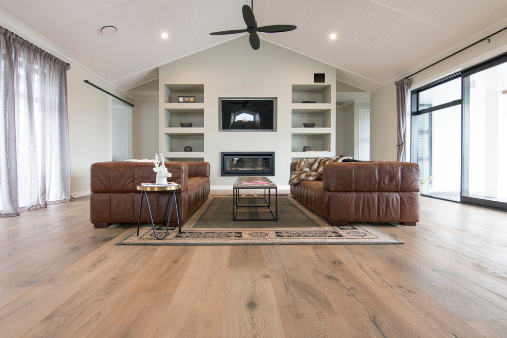Mid-sized country formal open concept living room in Auckland with medium hardwood floors, beige floor, grey walls, a ribbon fireplace and a wall-mounted tv.