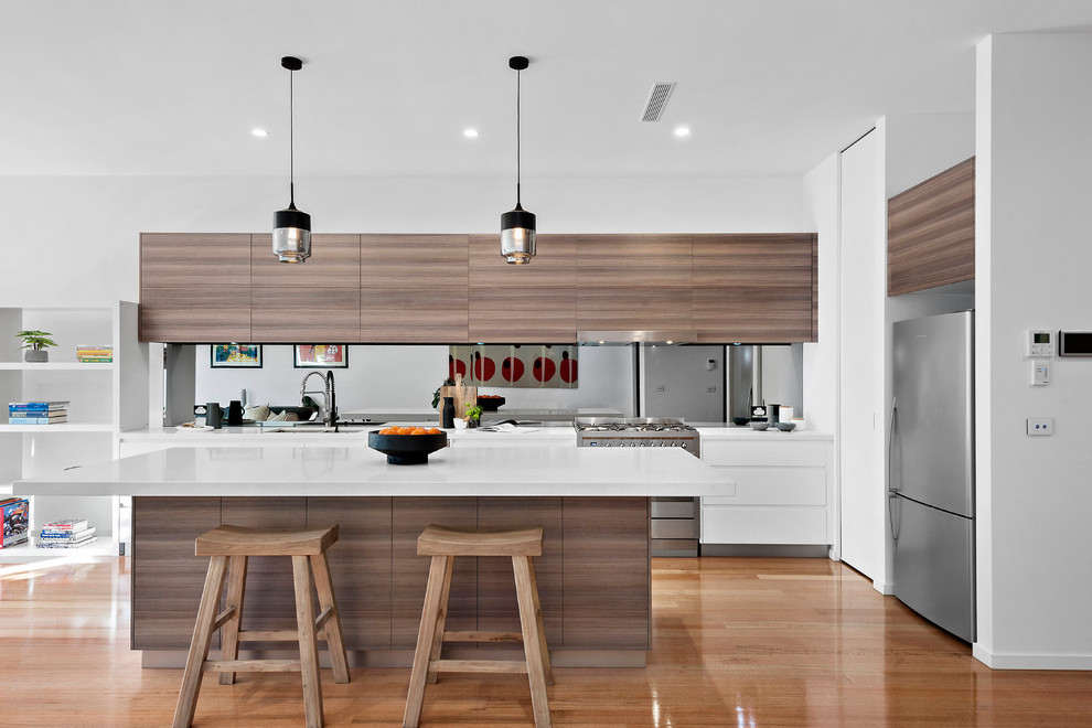 This is an example of a mid-sized contemporary open plan kitchen in Melbourne with a double-bowl sink, quartz benchtops, mirror splashback, stainless steel appliances, with island, white benchtop, flat-panel cabinets, dark wood cabinets and medium hardwood floors.