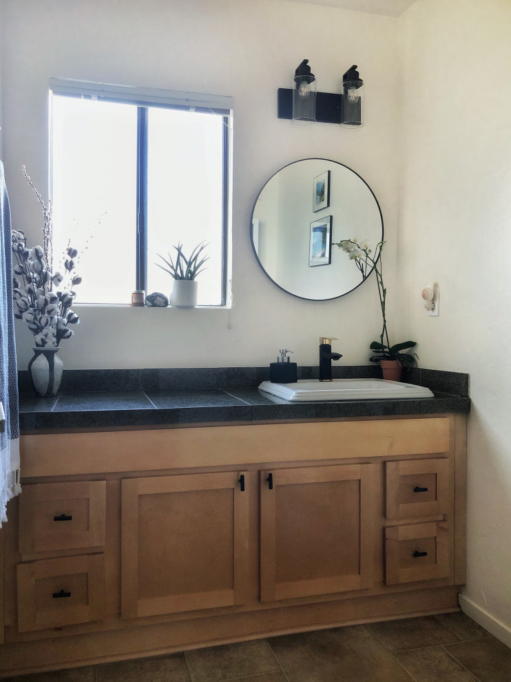 Small contemporary bathroom with shaker cabinets, light wood cabinets, a two-piece toilet, gray tile, white walls, linoleum floors, a drop-in sink, granite benchtops, brown floor, black benchtops, a single vanity and a built-in vanity.