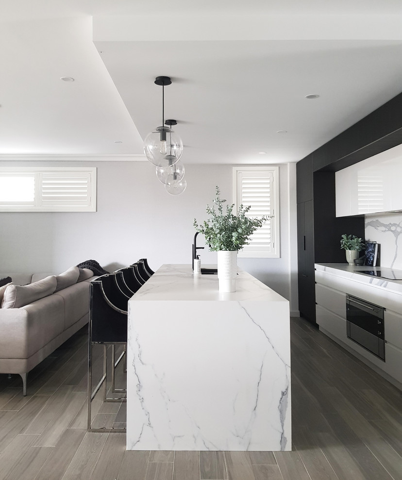 Inspiration for a large modern galley eat-in kitchen in Sydney with an undermount sink, white cabinets, white splashback, porcelain splashback, black appliances and with island.
