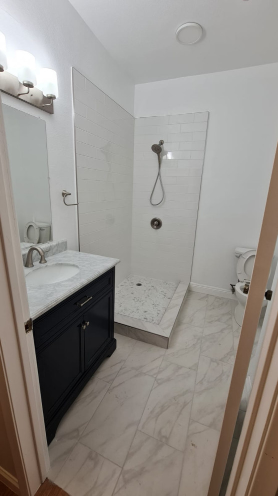 Example of a mid-sized master white tile and ceramic tile cement tile floor, yellow floor and single-sink doorless shower design in Los Angeles with black cabinets, a one-piece toilet, white walls, a drop-in sink, quartzite countertops, a hinged shower door, white countertops and a freestanding vanity