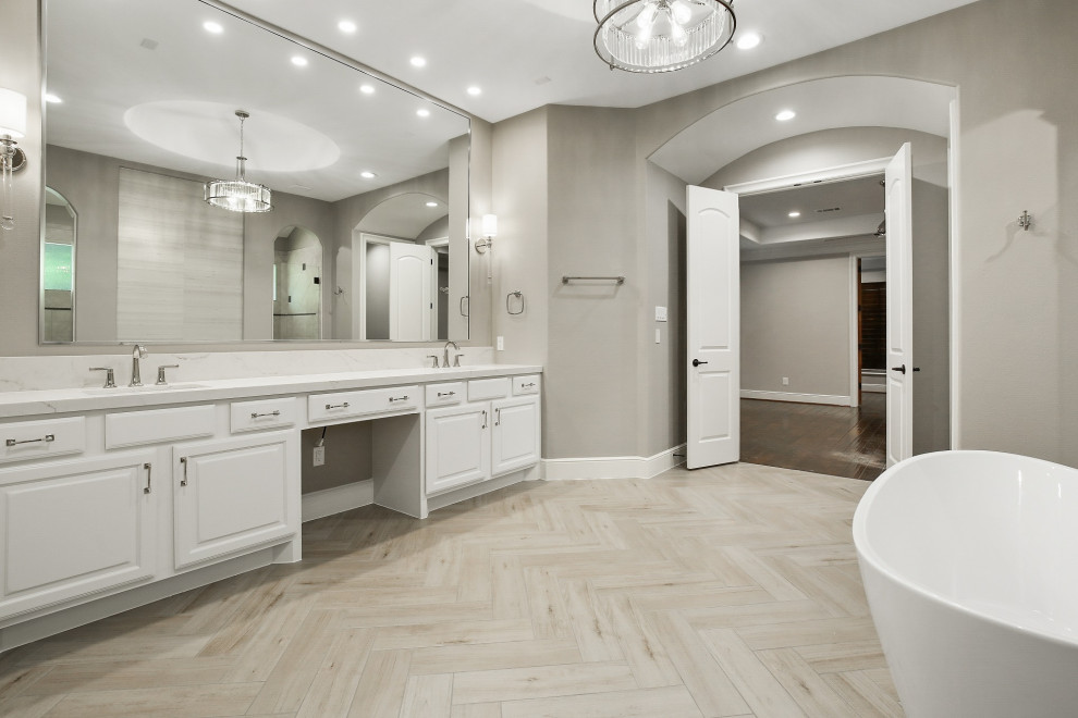 This is an example of a large transitional master wet room bathroom in Houston with raised-panel cabinets, white cabinets, a freestanding tub, beige tile, ceramic tile, grey walls, ceramic floors, an undermount sink, engineered quartz benchtops, grey floor, a hinged shower door, white benchtops, a double vanity, a built-in vanity, vaulted and wallpaper.