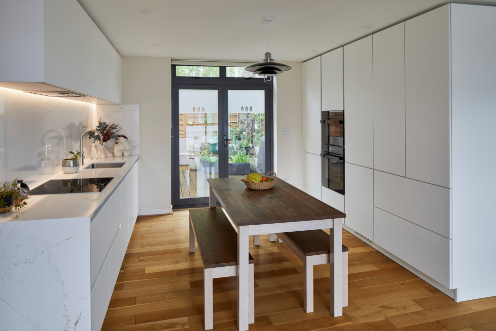 Idéer för att renovera ett mellanstort funkis vit linjärt vitt kök och matrum, med en undermonterad diskho, släta luckor, vita skåp, bänkskiva i kvarts, vitt stänkskydd, svarta vitvaror, mellanmörkt trägolv och brunt golv