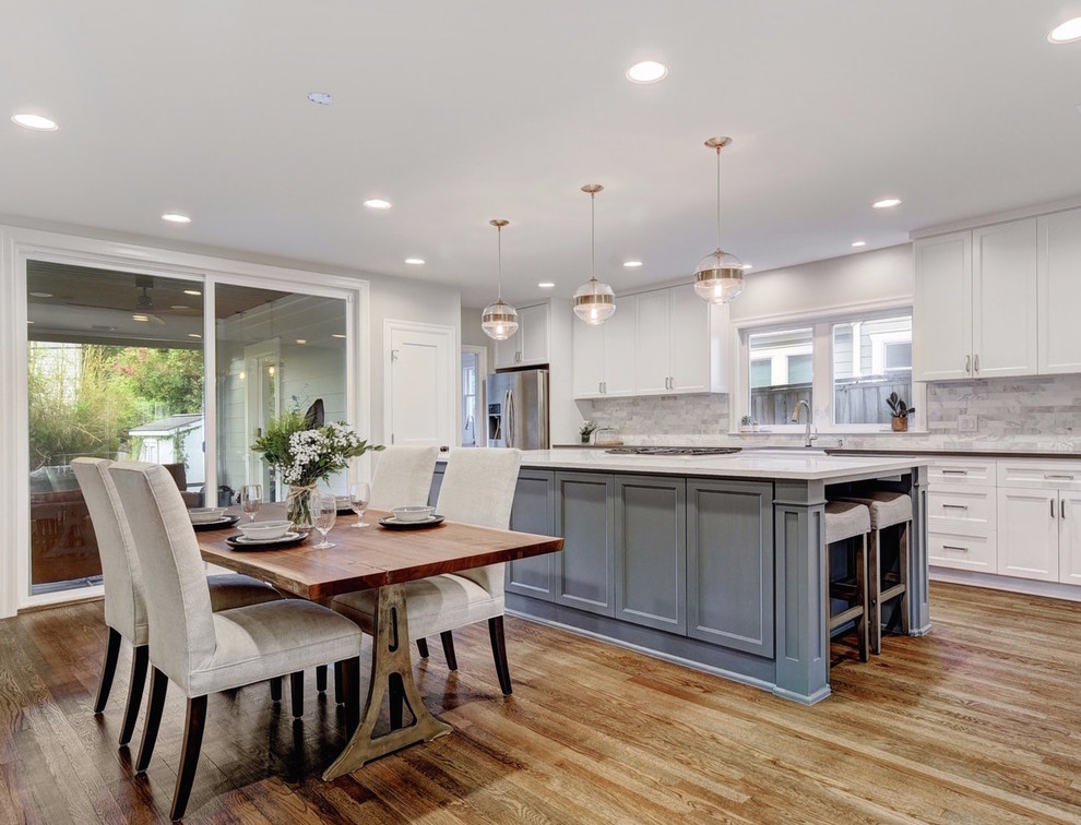 Design ideas for a large transitional galley eat-in kitchen in Austin with a farmhouse sink, shaker cabinets, white cabinets, quartz benchtops, white splashback, marble splashback, stainless steel appliances, light hardwood floors, with island, brown floor and white benchtop.