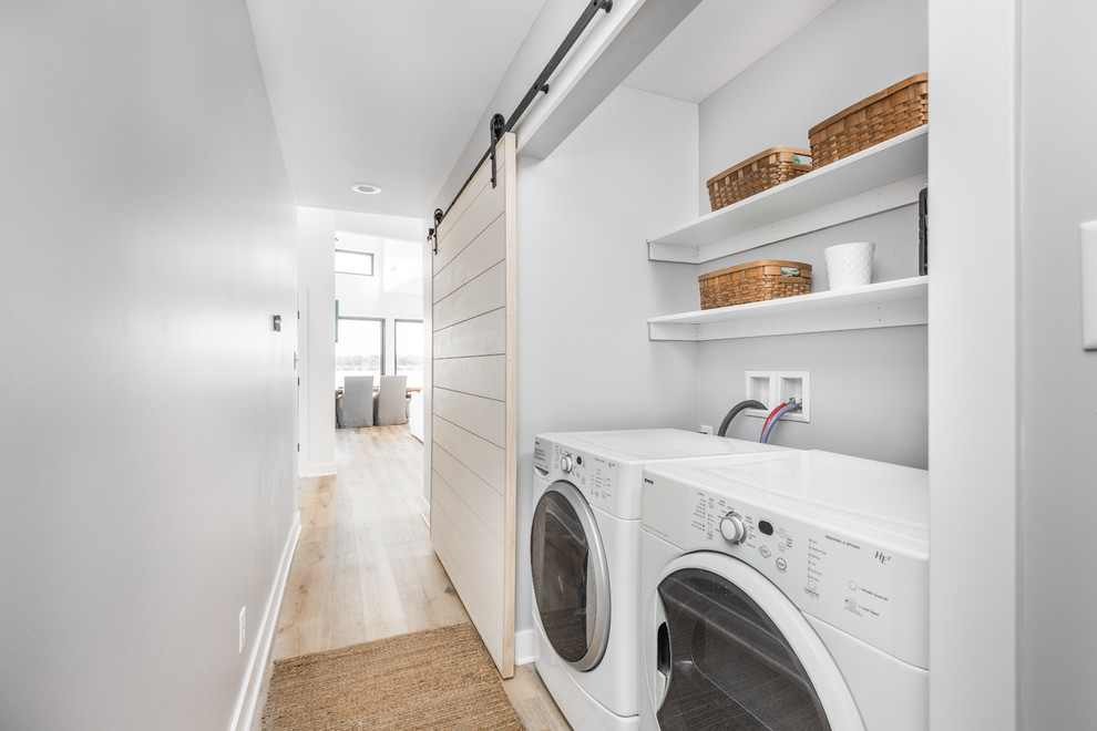Inspiration for a beach style single-wall laundry cupboard in Indianapolis with grey walls, light hardwood floors, a side-by-side washer and dryer and beige floor.