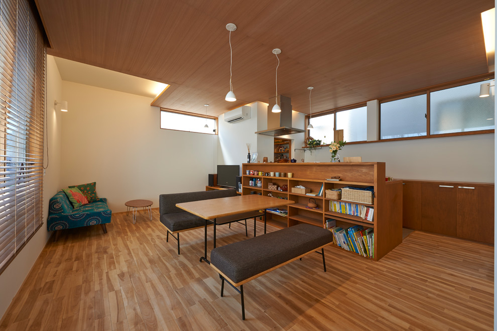 This is an example of an asian open concept living room in Tokyo with white walls, medium hardwood floors, a freestanding tv and brown floor.