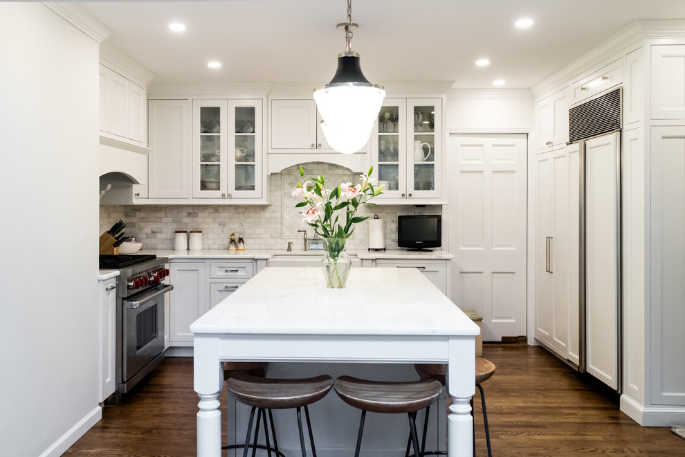Photo of a small transitional u-shaped kitchen in New York with a farmhouse sink, recessed-panel cabinets, white cabinets, quartzite benchtops, grey splashback, marble splashback, panelled appliances, dark hardwood floors, with island, brown floor and white benchtop.