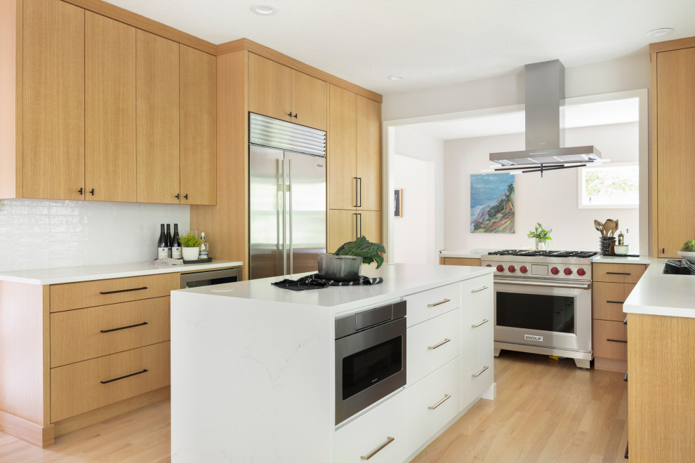 Design ideas for a mid-sized contemporary u-shaped open plan kitchen in Portland with an undermount sink, flat-panel cabinets, medium wood cabinets, quartz benchtops, white splashback, cement tile splashback, stainless steel appliances, light hardwood floors, with island and white benchtop.