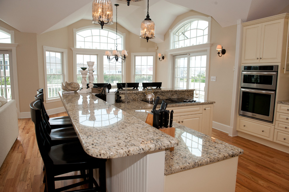 Example of a large transitional light wood floor open concept kitchen design with an undermount sink, raised-panel cabinets, beige cabinets, granite countertops, multicolored backsplash, mosaic tile backsplash, stainless steel appliances and a peninsula
