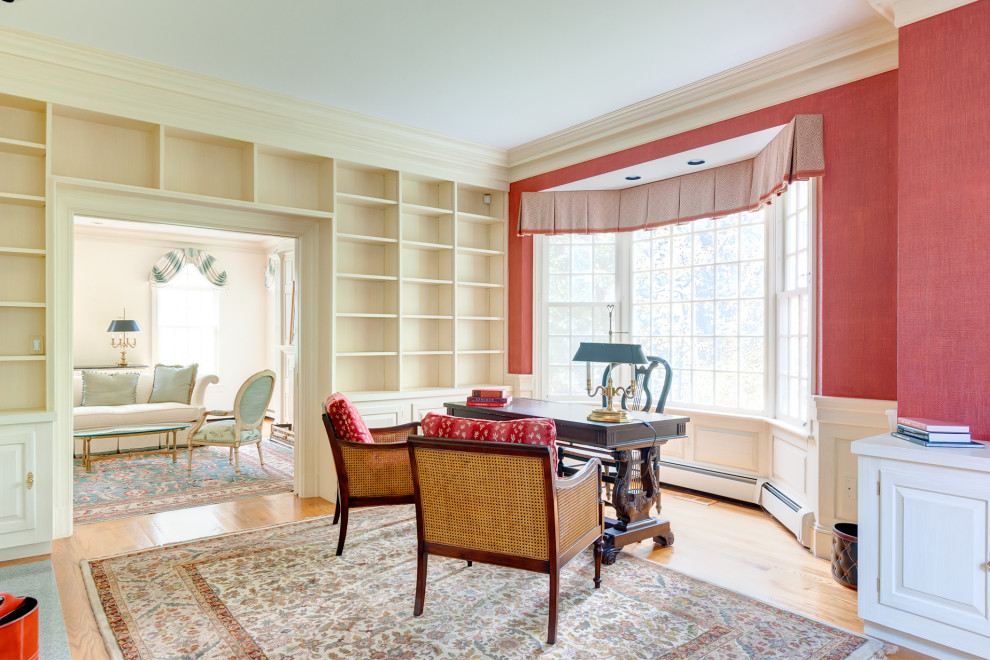 Inspiration for a large home office in Boston with a library, red walls, medium hardwood floors, a standard fireplace, a wood fireplace surround and a freestanding desk.