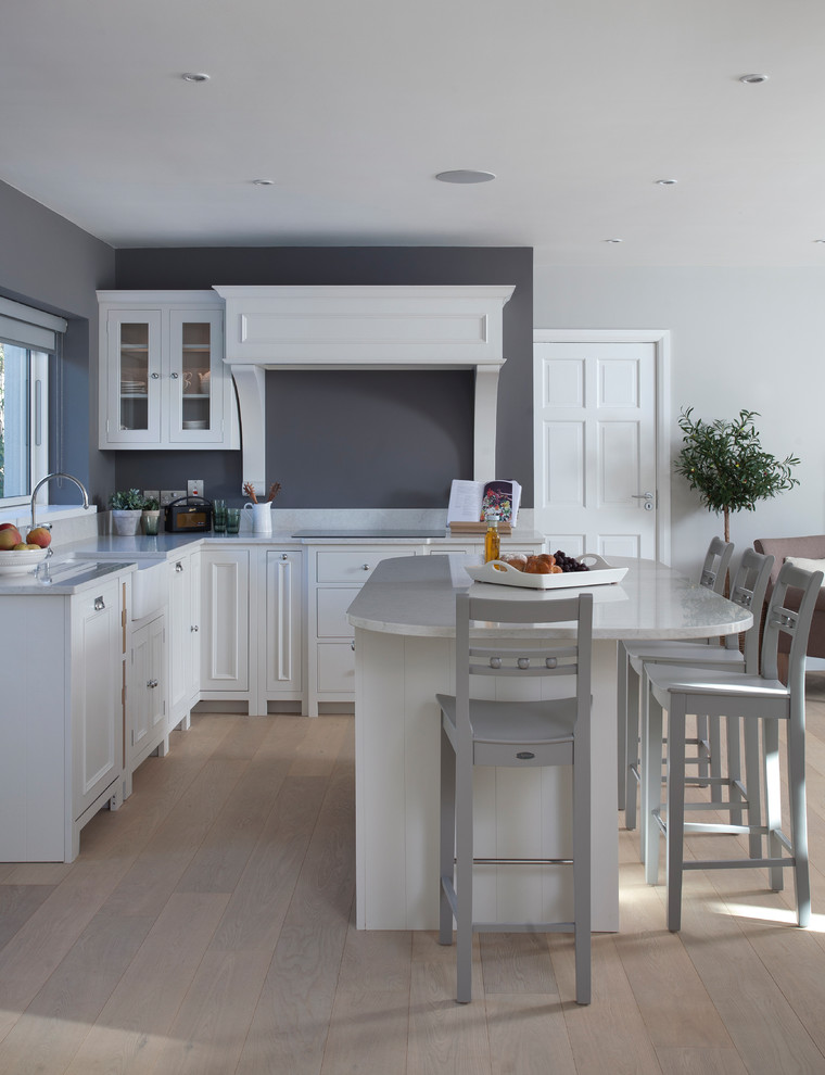 Photo of a mid-sized transitional l-shaped separate kitchen in Dublin with recessed-panel cabinets, white cabinets, grey splashback, light hardwood floors, with island and beige floor.
