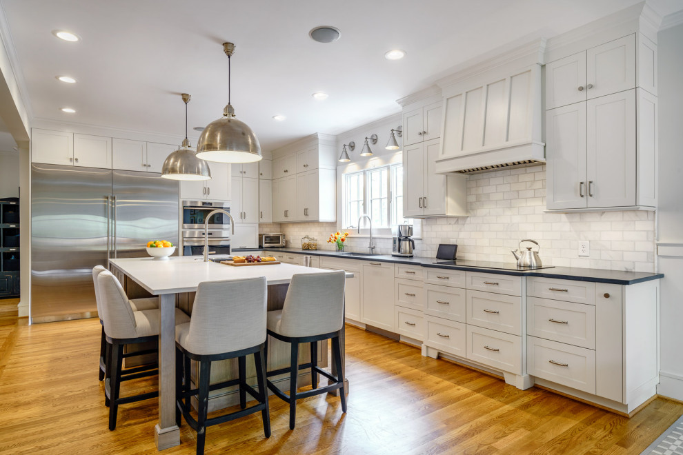 Large transitional galley medium tone wood floor and brown floor eat-in kitchen photo with an undermount sink, shaker cabinets, white cabinets, quartz countertops, white backsplash, marble backsplash, stainless steel appliances, an island and white countertops