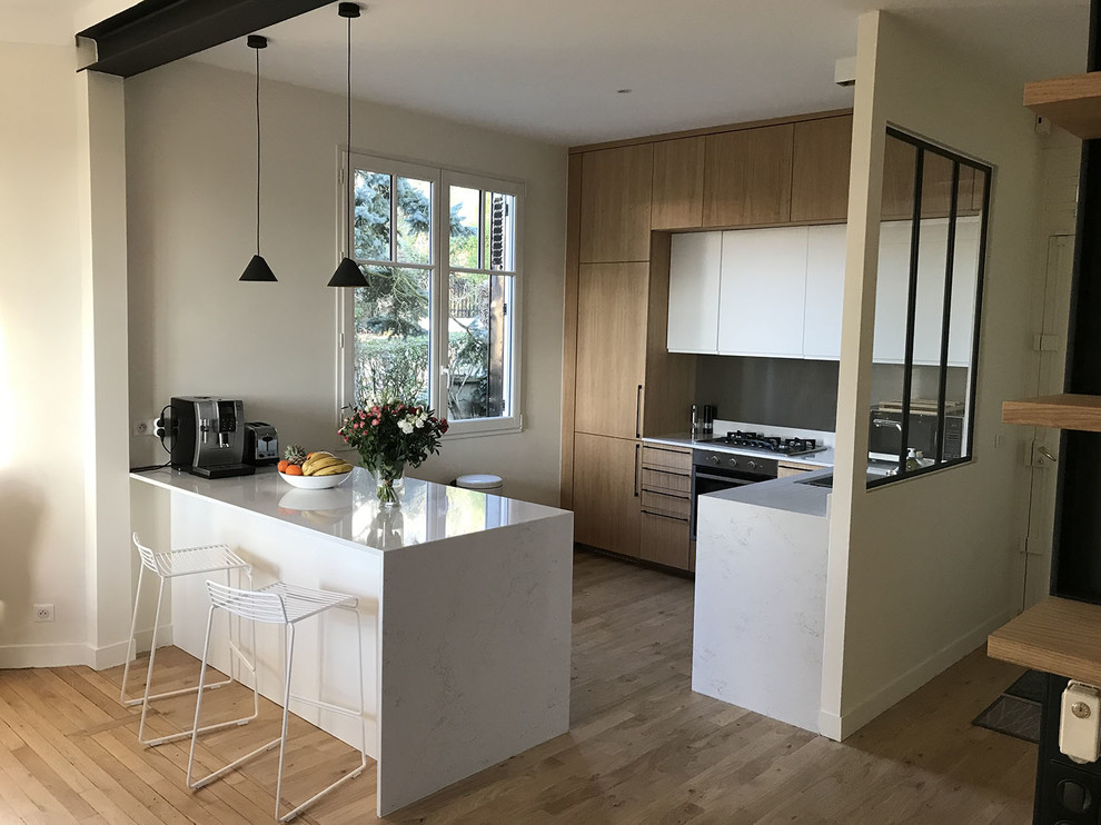Photo of a large contemporary l-shaped open plan kitchen in Paris with light wood cabinets, quartzite benchtops, with island, white benchtop, an integrated sink, beaded inset cabinets, metallic splashback, metal splashback, panelled appliances and light hardwood floors.