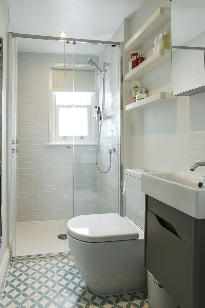 Inspiration for a small contemporary bathroom in London with flat-panel cabinets, grey cabinets, a one-piece toilet, white tile, ceramic tile, white walls, cement tiles, multi-coloured floor, a sliding shower screen, a corner shower and a console sink.