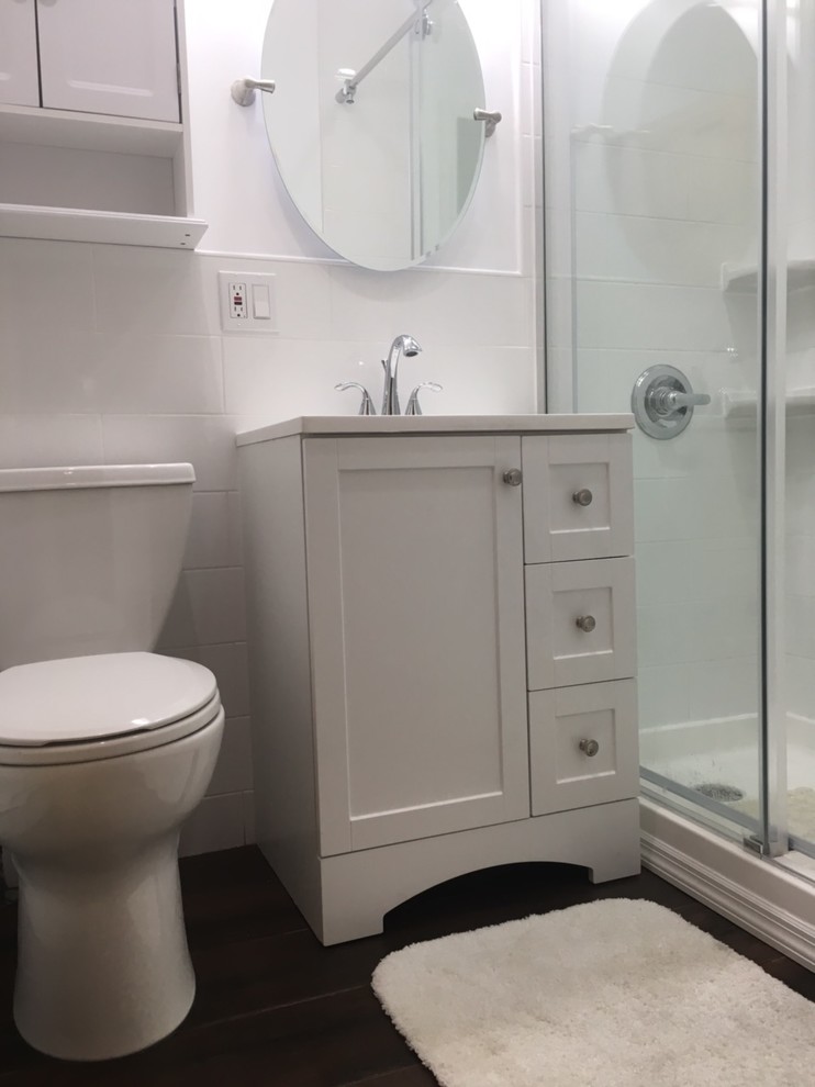 Design ideas for a small transitional 3/4 bathroom in New York with shaker cabinets, grey cabinets, an alcove shower, a two-piece toilet, white tile, ceramic tile, black walls, porcelain floors, an integrated sink, solid surface benchtops, black floor and a sliding shower screen.