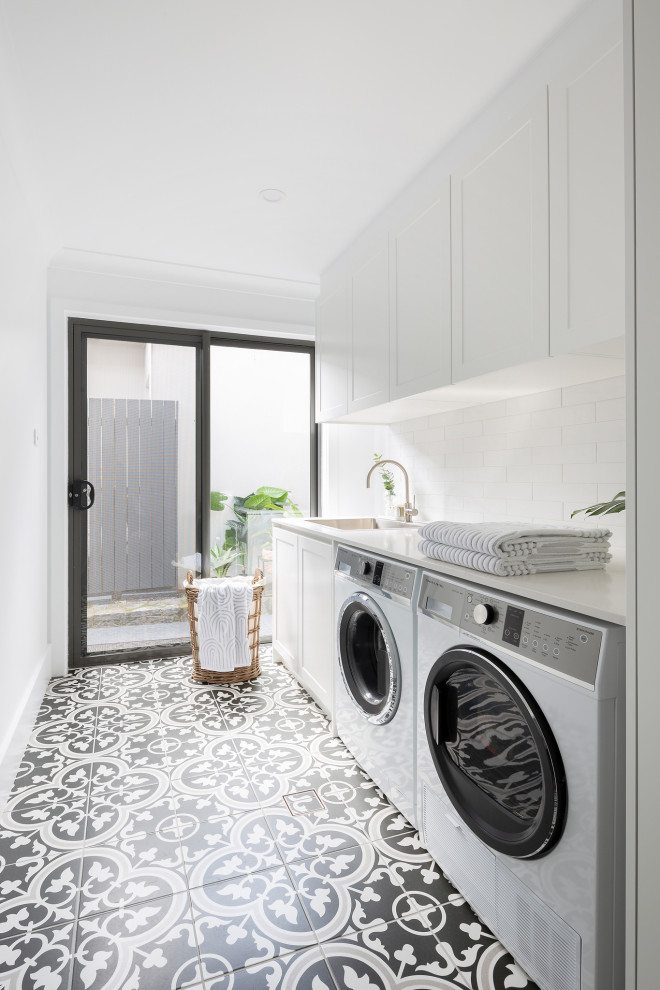 Photo of a modern utility room in Canberra - Queanbeyan with an integrated sink, shaker cabinets, white cabinets, engineered stone countertops, white splashback, metro tiled splashback, yellow walls, porcelain flooring, a side by side washer and dryer, blue floors and white worktops.