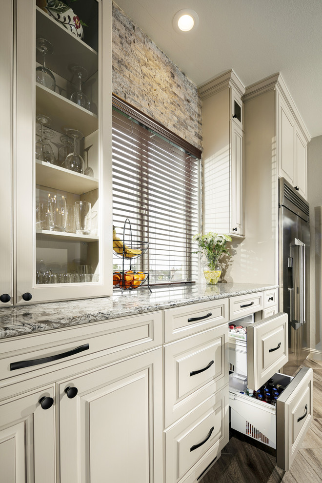 Inspiration for a large transitional l-shaped porcelain tile and brown floor eat-in kitchen remodel in Orlando with an undermount sink, raised-panel cabinets, beige cabinets, quartz countertops, multicolored backsplash, travertine backsplash, stainless steel appliances, an island and multicolored countertops