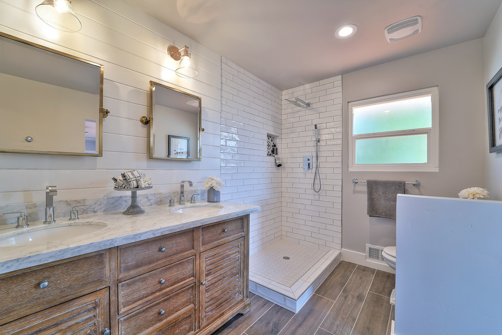 Photo of a mid-sized country master bathroom in San Francisco with furniture-like cabinets, distressed cabinets, a corner shower, a two-piece toilet, white tile, porcelain tile, grey walls, porcelain floors, an undermount sink, marble benchtops and brown floor.
