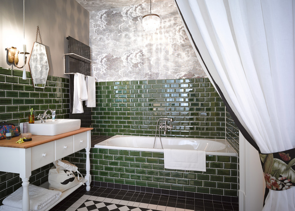 Photo of a mid-sized eclectic bathroom in Berlin with a vessel sink, white cabinets, wood benchtops, an alcove tub, a shower/bathtub combo, green tile, subway tile, grey walls and flat-panel cabinets.
